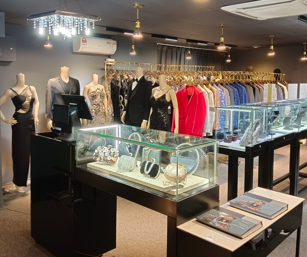 Interior of Shingary Diamonia boutique displaying luxury designer clothing, including suits, gowns, and accessories, along with high-end jewelry and handbags in glass cases.